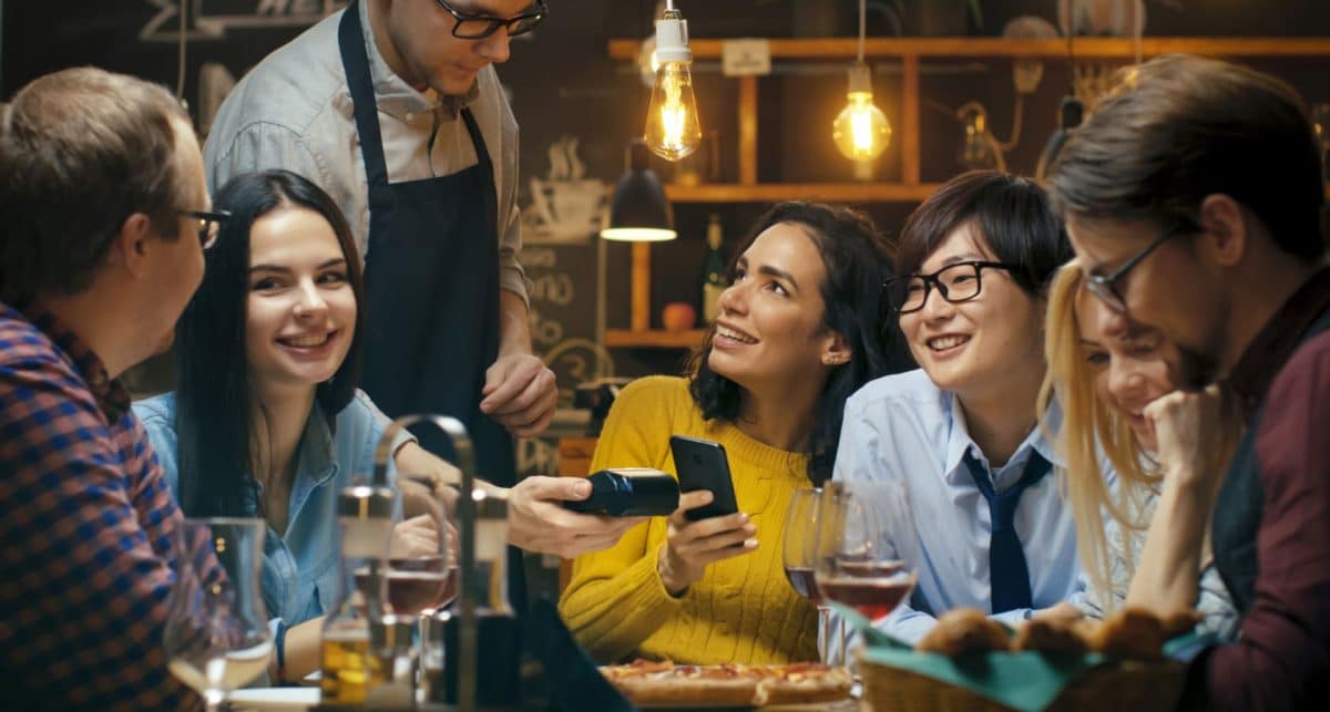 a group of diners, with one paying for their meal using a phone