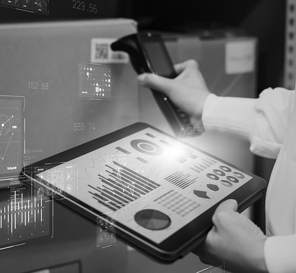 A worker in a warehouse uses a scanner to identify a package and review the package information on a tablet.