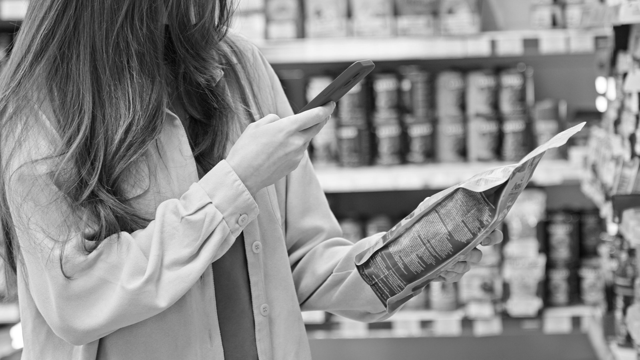 Woman scanning a product with a smartphone in a supermarket aisle.